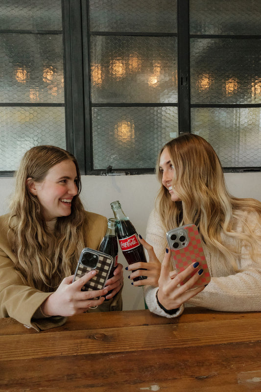 Two girls drinking soda holding phone cases with gingham and checkered patterns
