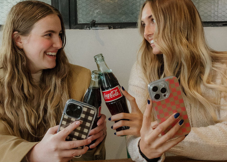 girlies doing cheers with coke bottles while holding colorful phone cases